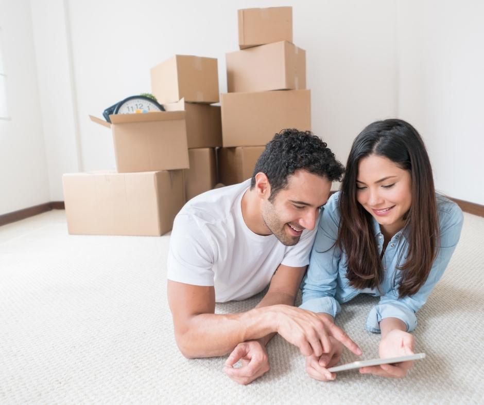 Couple lying on the floor of their new home, with moving boxes stacked behind them.