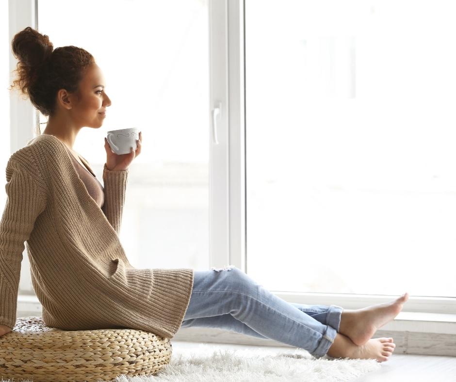 Woman drinking coffee from a decorative coffee mug while looking out the window. 